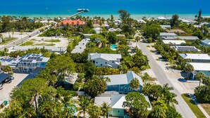 An aerial view of a coastal residential area with houses, a dock, and a bridge in the background. - Mermaid Cove: Updated Forida Cottage w/pool, hot tub (Anna Maria)