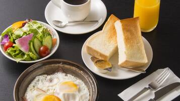 Una mesa de desayuno con tostadas, huevos, ensalada, café y jugo de naranja.