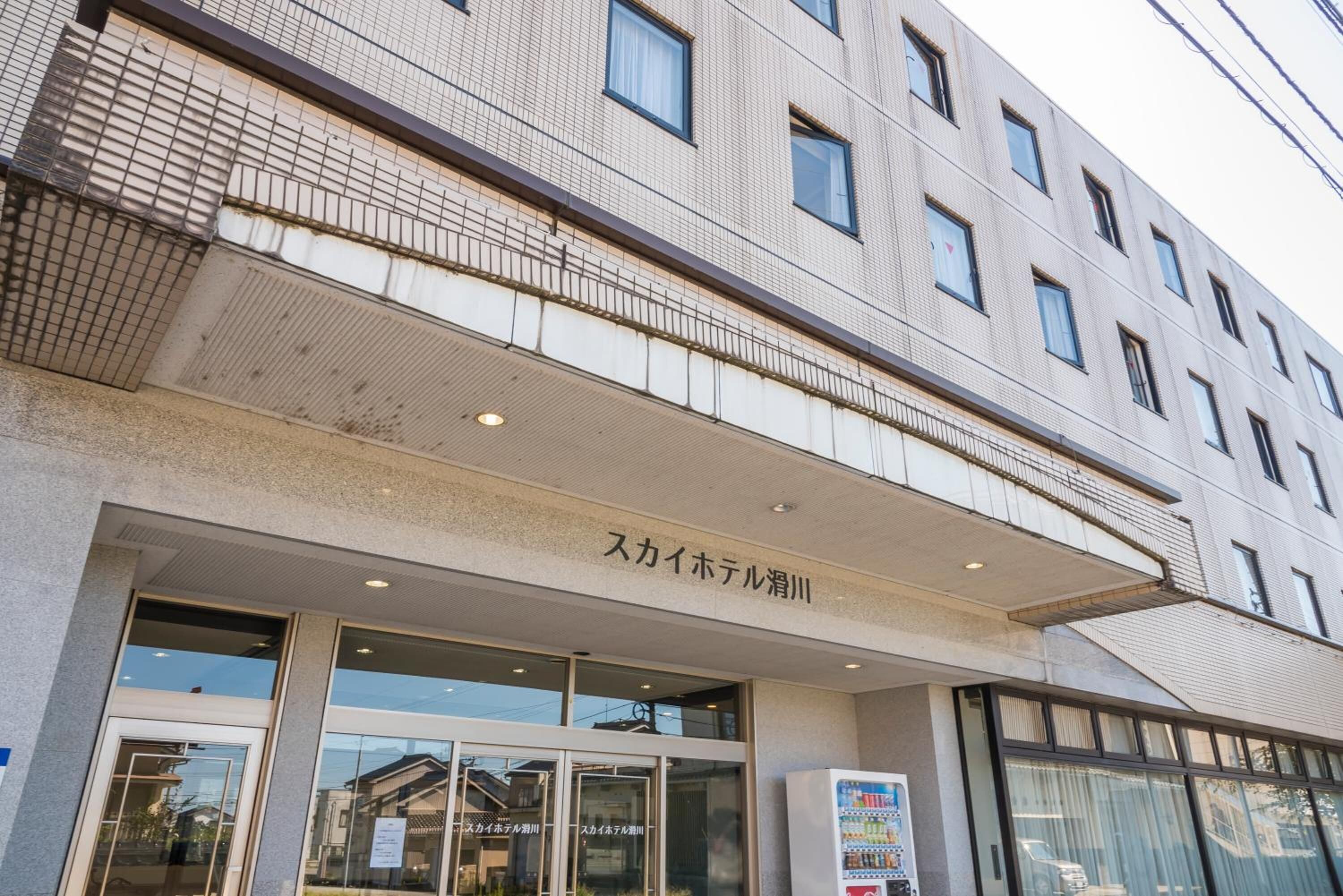 A hotel entrance with a sign in Japanese, large windows, and a vending machine outside.