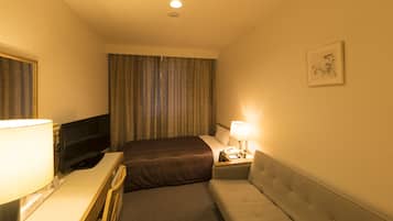 Una habitación de hotel con cama, escritorio con lámpara, televisor, mesita de noche con lámpara y un cuadro en la pared.