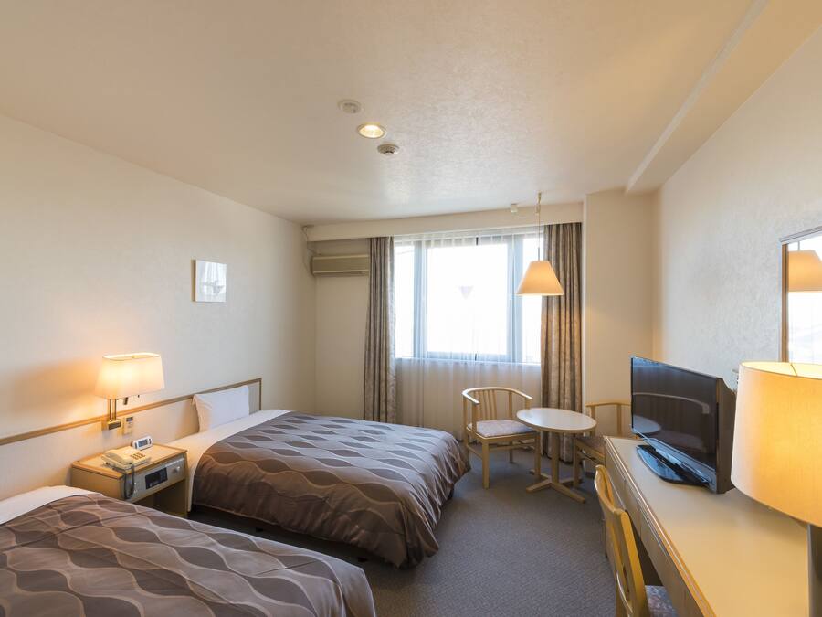 Ett hotellrum med två sängar, ett skrivbord med en tv, en stol och en lampa.