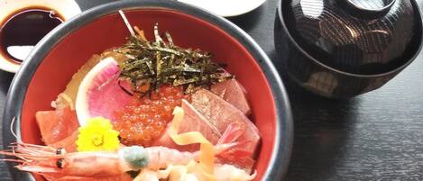 A bowl of sashimi with various seafood, including shrimp, fish, and roe, accompanied by small dishes of soy sauce and wasabi.