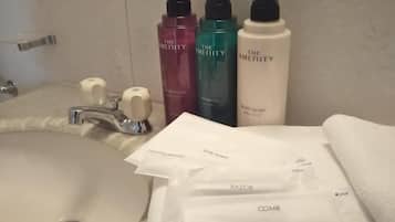 Een badkamermeubel met een wastafel, drie flessen toiletartikelen van The Amenity, een witte handdoek en een douchehanddoek.