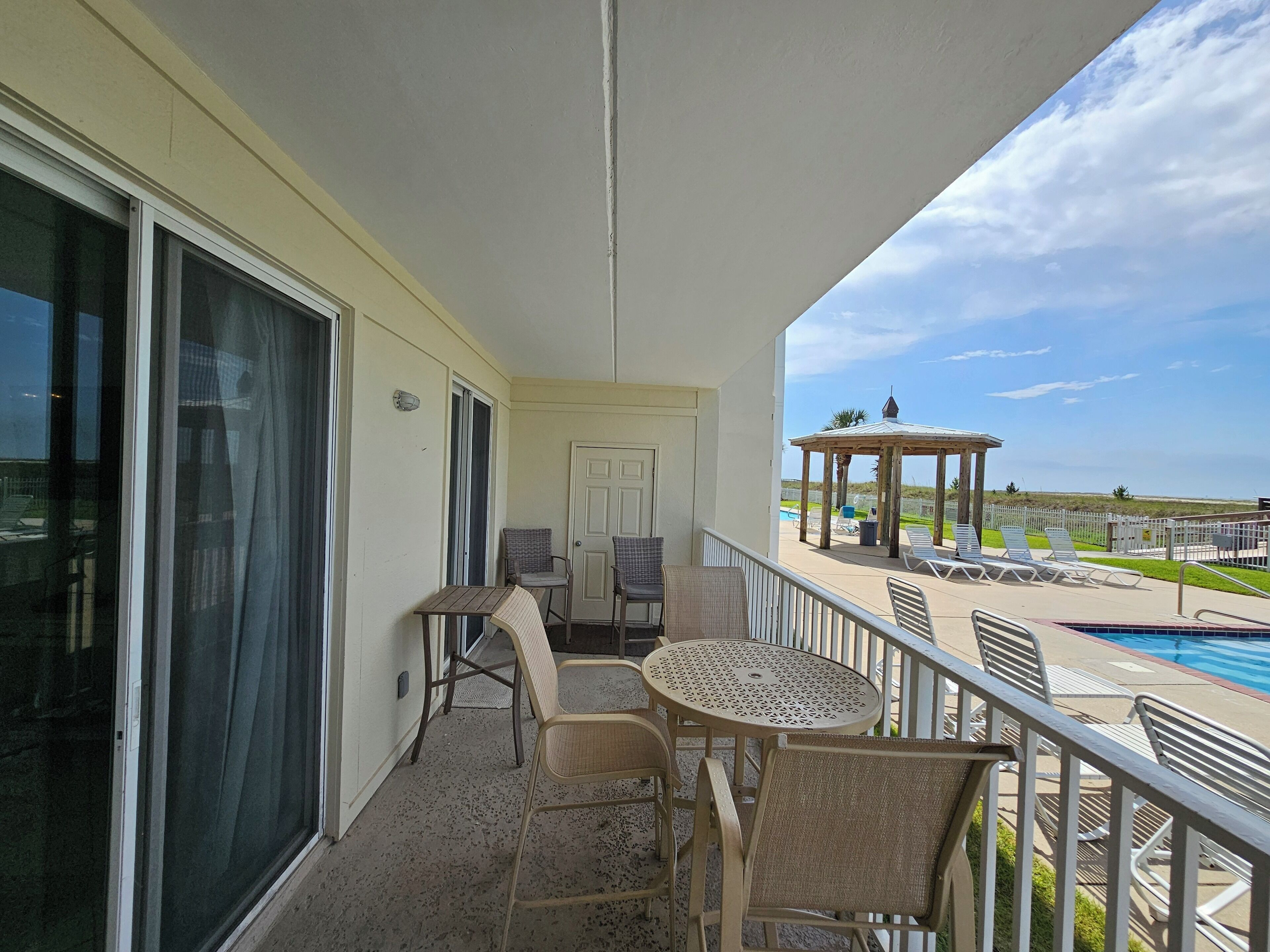 Een balkon met een tafel, stoelen, een deur en uitzicht op een zwembad en strand.