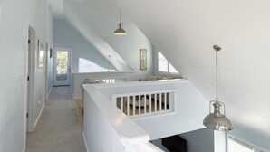 Un hall d’entrée spacieux avec un plafond haut, un escalier menant à une mezzanine, et une suspension lumineuse.