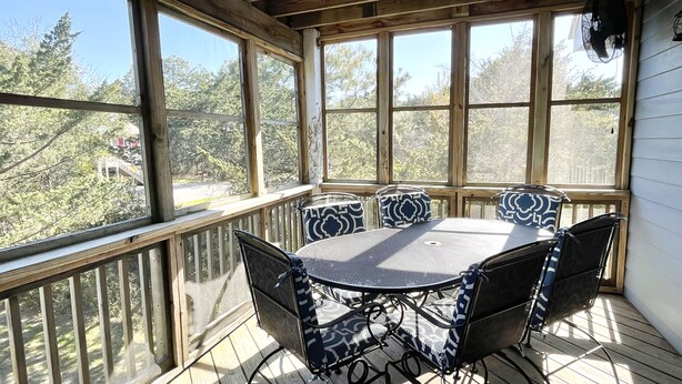 Un patio extérieur abrité, doté d’une table ronde et de quatre chaises, de grandes fenêtres et d’une terrasse en bois.