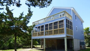 Une maison à deux étages avec un balcon, entourée d’arbres et d’une cour verdoyante.