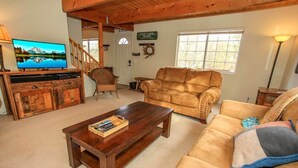 Un salón acogedor con un mueble de madera para el equipo de entretenimiento, un sofá de cuero y un televisor que muestra un paisaje de montaña.