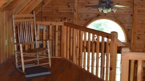 A wooden interior with a wooden staircase, a ceiling fan, and a window with a view of trees.