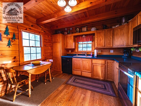 Interior de una cabaña de madera con cocina, mesa de comedor y ventana con vistas.