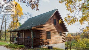 A wooden cabin with a porch, a small attached structure, and a gravel driveway.