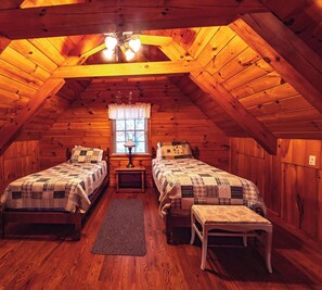 Um quarto de sótão aconchegante com duas camas, uma janela com cortinas e um ventilador de teto.