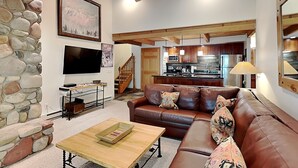 A modern living room with a stone wall, a brown leather sofa, a wooden coffee table, and a kitchen in the background. - 🌲Timberline C3G Deluxe 1-Bedroom + Loft ~Hot Tub~Pool~WiFi~Ski-in/out~Local Shuttle🌲 (Snowmass Village)