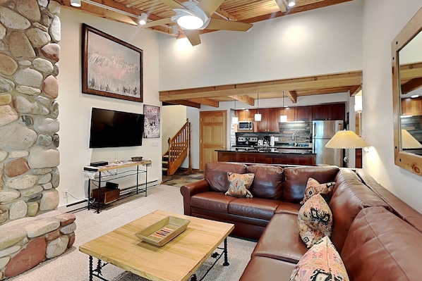 A modern living room with a stone wall, a brown leather sofa, a wooden coffee table, and a kitchen in the background. - 🌲Timberline C3G Deluxe 1-Bedroom + Loft ~Hot Tub~Pool~WiFi~Ski-in/out~Local Shuttle🌲 (Snowmass Village)