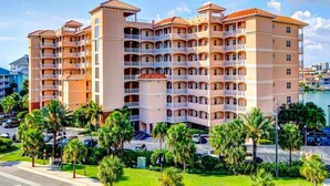 A multi-story hotel with balconies, a parking lot, and palm trees.