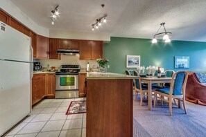 A kitchen with wooden cabinets, a refrigerator, an oven, and a dining area with a table and chairs. - Greystone Lodge 214 Ski-in/Out by Acer Vacations (Whistler)