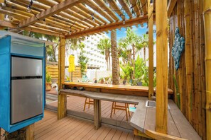 Ein Außenbereich mit Terrasse, einer Holz-Pergola, einem Edelstahl-Kühlschrank und einer Sitzbank.