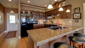 Una cocina con encimeras de granito, electrodomésticos de acero inoxidable, armarios de madera e iluminación colgante.