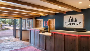 A reception area with a wooden reception desk, a sign for Timberline Condominiums, and a view of the outside. - 🌲Timberline 115 Studio Deluxe ~ Hot Tub~Pool~WiFi~Ski-in/out~Local Shuttle🌲 (Snowmass Village)