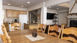A dining area with a wooden table and chairs, a kitchen in the background, a staircase, and a fireplace. - Spacious Town Home with Ski-In/Ski-Out Access (Whitefish)