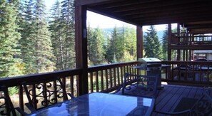A wooden deck with a glass table and chairs, overlooking a forested area. - Spacious Town Home with Ski-In/Ski-Out Access (Whitefish)