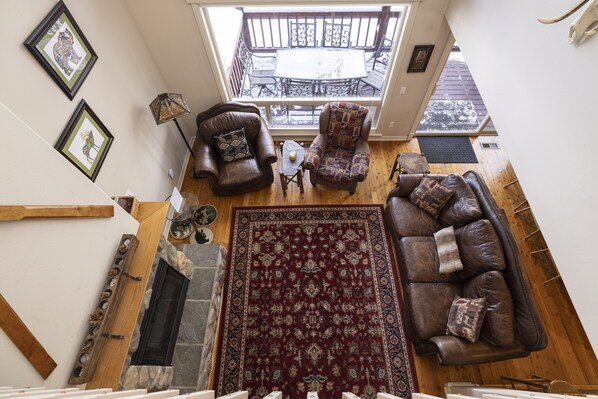 A cozy living room with a fireplace, a large rug, and a view of the balcony. - Spacious Town Home with Ski-In/Ski-Out Access (Whitefish)