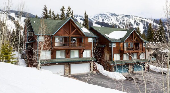 A wooden lodge with multiple balconies and a view of snow-covered mountains.
