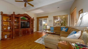 A spacious living room with a wooden entertainment center, a beige sofa, and a ceiling fan. - Tropical Villa w/Beach Club Access ★Quiet Location★Bikes and Beach Gear★Walk to Restaurants (Kamuela)