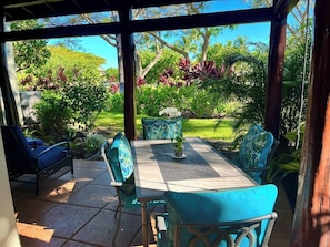 Relax in a serene outdoor setting with a covered patio featuring a round table and comfortable seating surrounded by lush greenery.