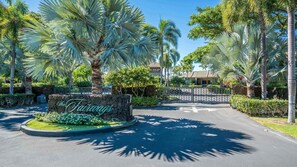 A gated entrance with a sign reading 'The Fairways,' surrounded by palm trees and a stone wall. - Tropical Villa w/Beach Club Access ★Quiet Location★Bikes and Beach Gear★Walk to Restaurants (Kamuela)