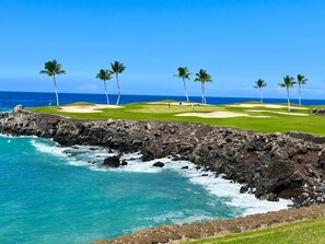A coastal golf course with a rocky shoreline, palm trees, and a clear view of the ocean.