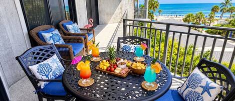 Un balcon agrémenté de mobilier d’extérieur, une table avec de la nourriture et des boissons, et une vue sur l’océan.