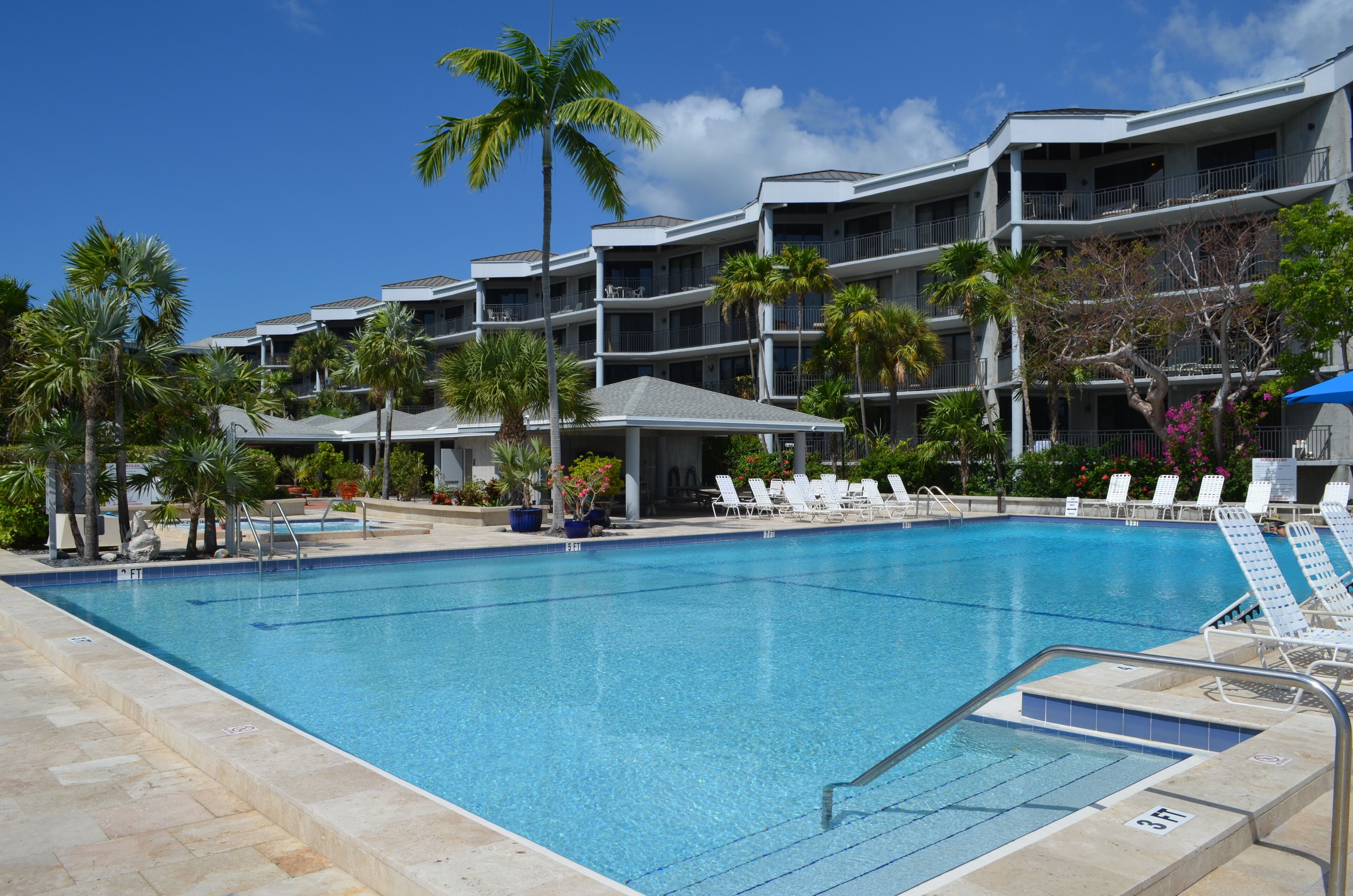 A hotel with a swimming pool, palm trees, and a clear blue sky.