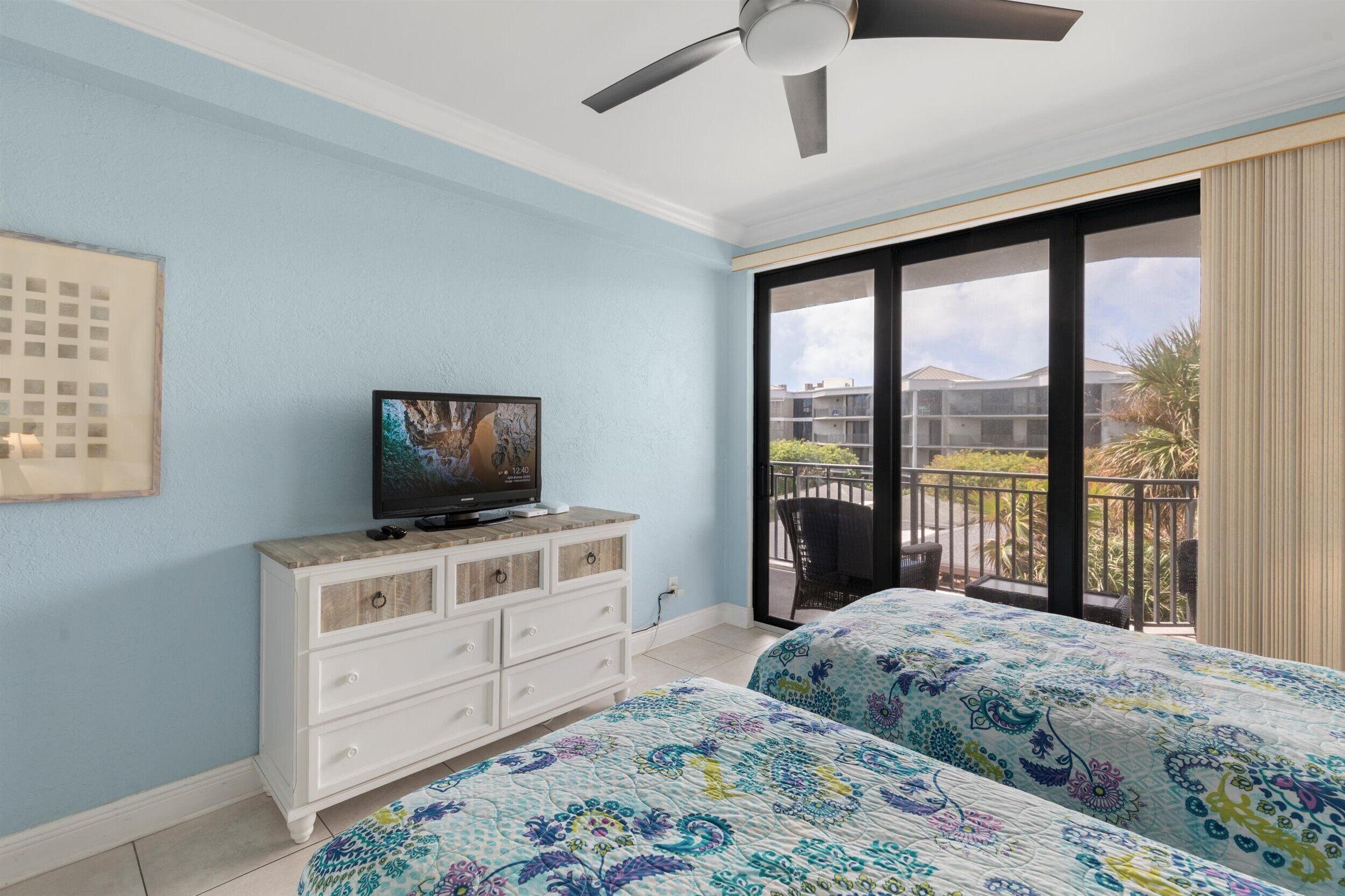 Un dormitorio con dos camas, un televisor en una cómoda y un balcón con mobiliario exterior.