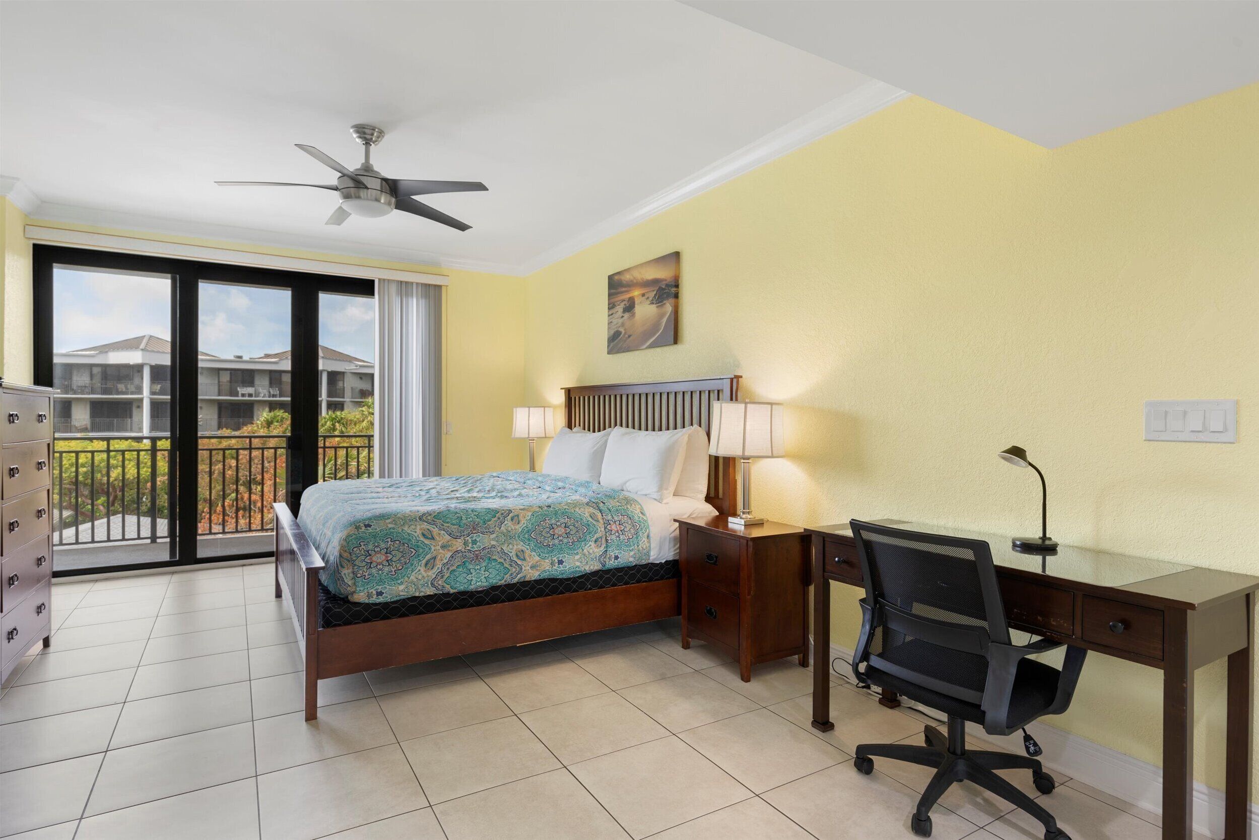 A hotel room with a bed, desk, chair, and a balcony with a view.