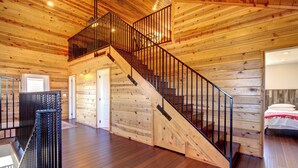 Interior de madera con una escalera, paredes de madera y una cama con una manta roja.