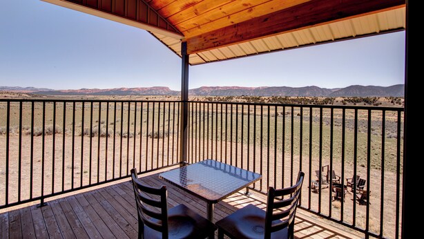Una terraza de madera con una mesa y sillas, con vistas a un paisaje desértico y montañas a lo lejos.