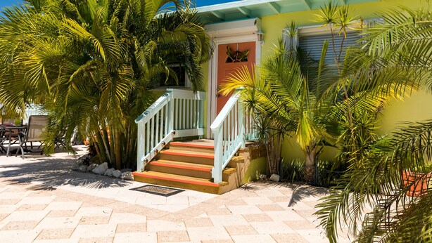Une maison avec un escalier menant à une porte, entourée de palmiers et dotée d’une terrasse carrelée.