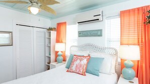 Une chambre à coucher avec un lit, une tête de lit blanche, deux tables de chevet avec des lampes, un climatiseur et un ventilateur de plafond.