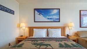 Une chambre d’hôtel avec un lit, deux lampes de chevet, un tableau encadré représentant un skieur et un tableau encadré représentant une forêt.