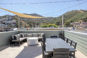 A rooftop patio with a sectional sofa, a round coffee table, and a dining table with chairs.