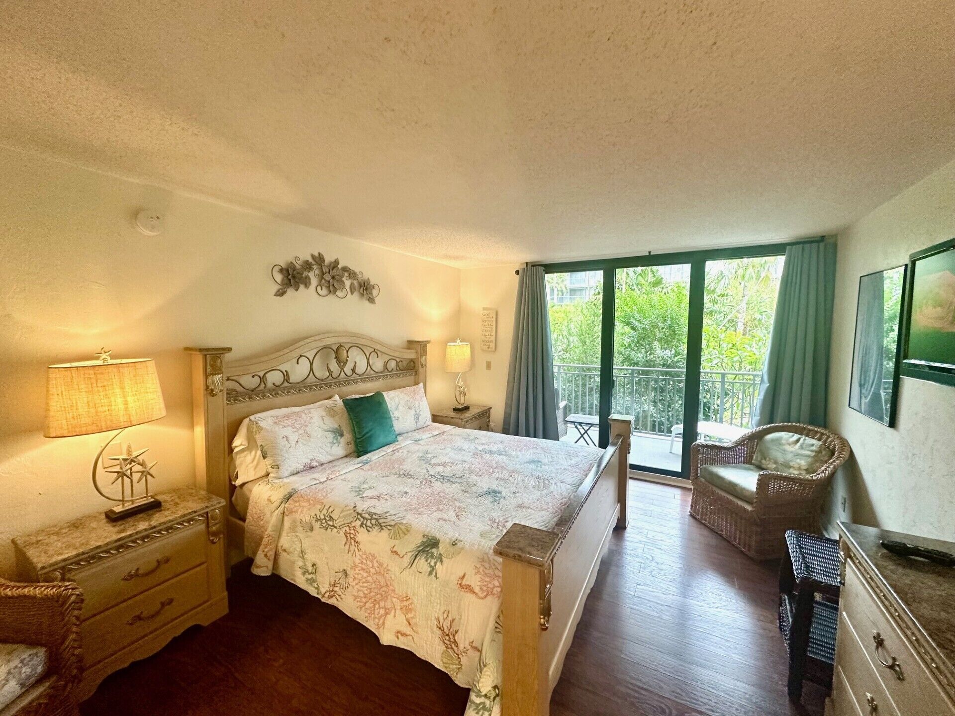 Ein Schlafzimmer mit Bett, Nachttischen, einem Sessel, einer Kommode und einem Balkon mit Blick auf Grünflächen.