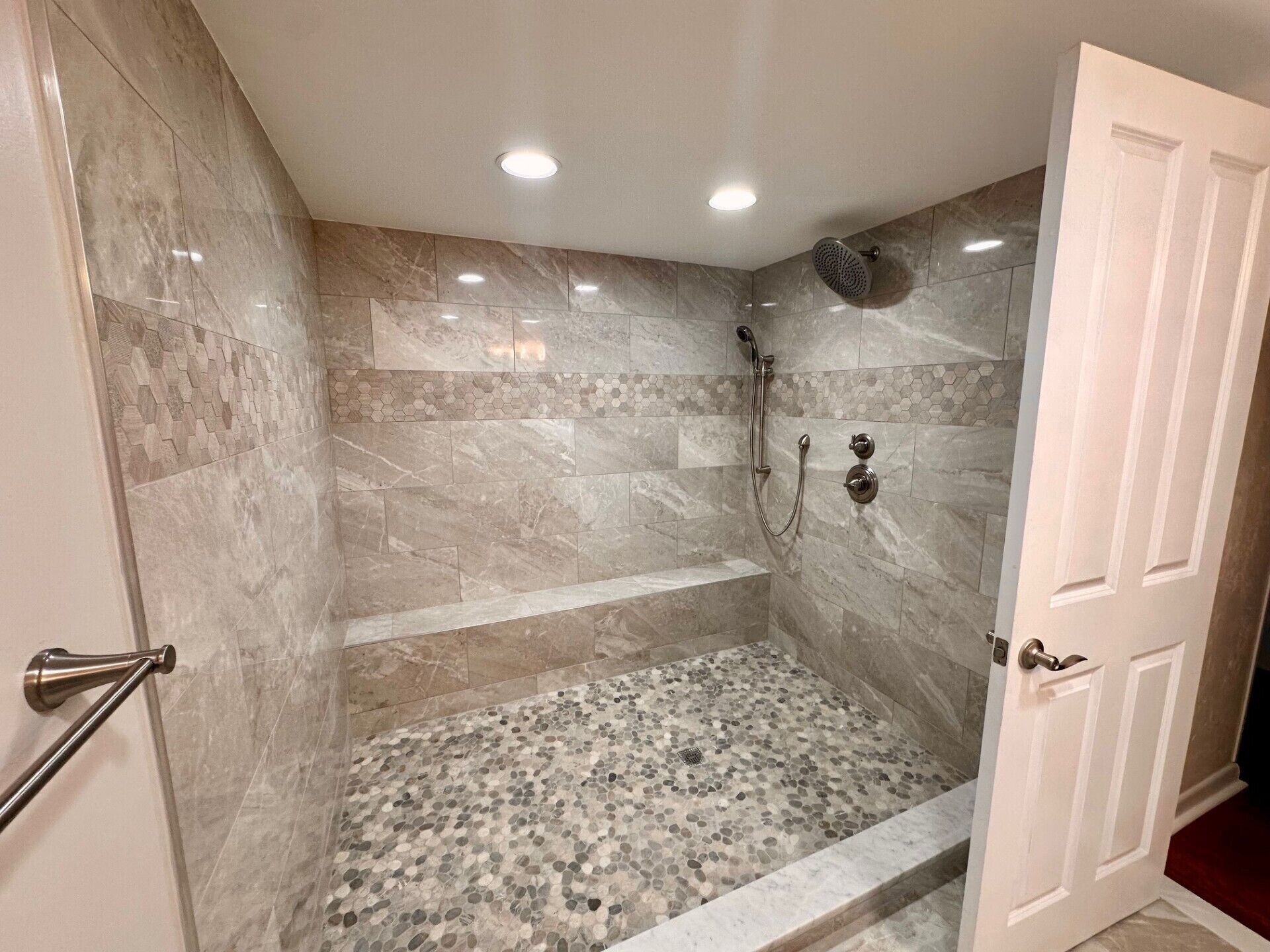 A walk-in shower with a tiled floor, a showerhead, and a handrail.