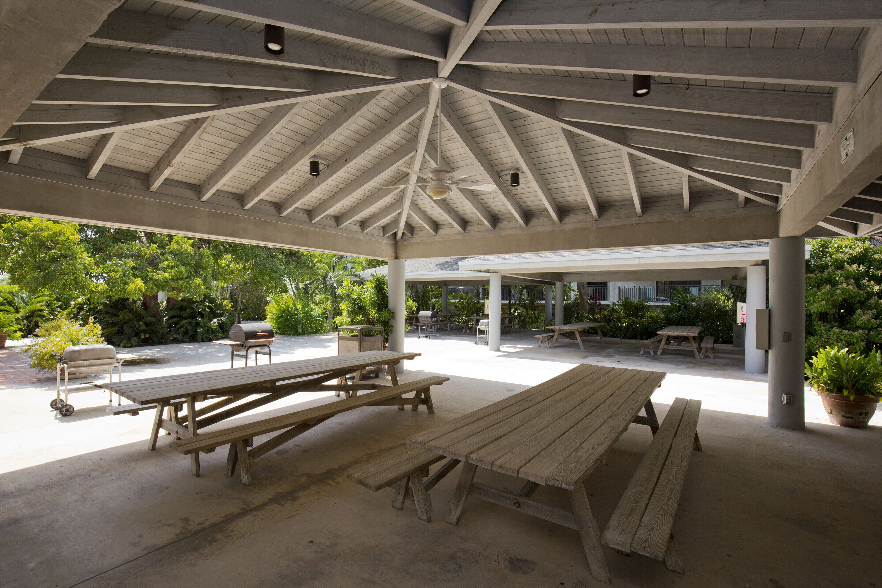 Un espace pique-nique extérieur abrité, équipé de plusieurs tables en bois et d’un barbecue.