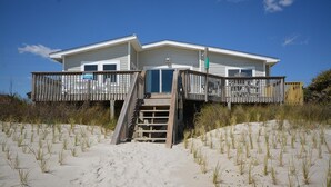Una casa frente a la playa con una terraza de madera y una escalera que lleva a un porche cubierto.