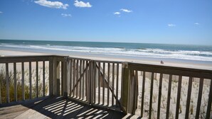 Una terraza de madera con vista a una playa, olas y un cielo despejado.