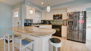 Una cocina moderna con una isla central, electrodomésticos de acero inoxidable y diseño de muebles blancos.
