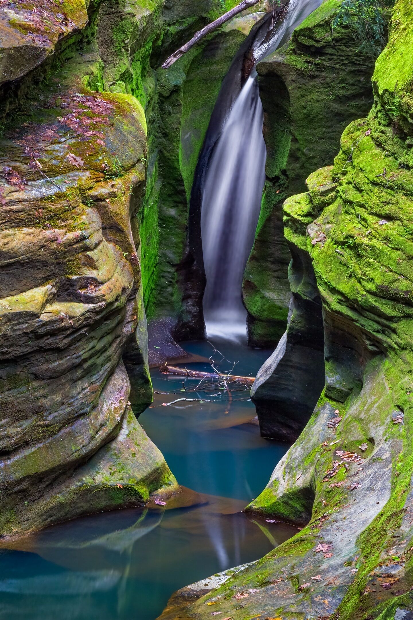 A waterfall cascading through a narrow, rocky gorge with moss-covered walls.