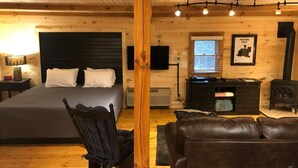 A cozy log cabin room with a bed, a leather sofa, a chair, and a fireplace. - The Retreat - Cozy studio cabin - Hot Tub, Firepit, pond, natural playground (Logan)