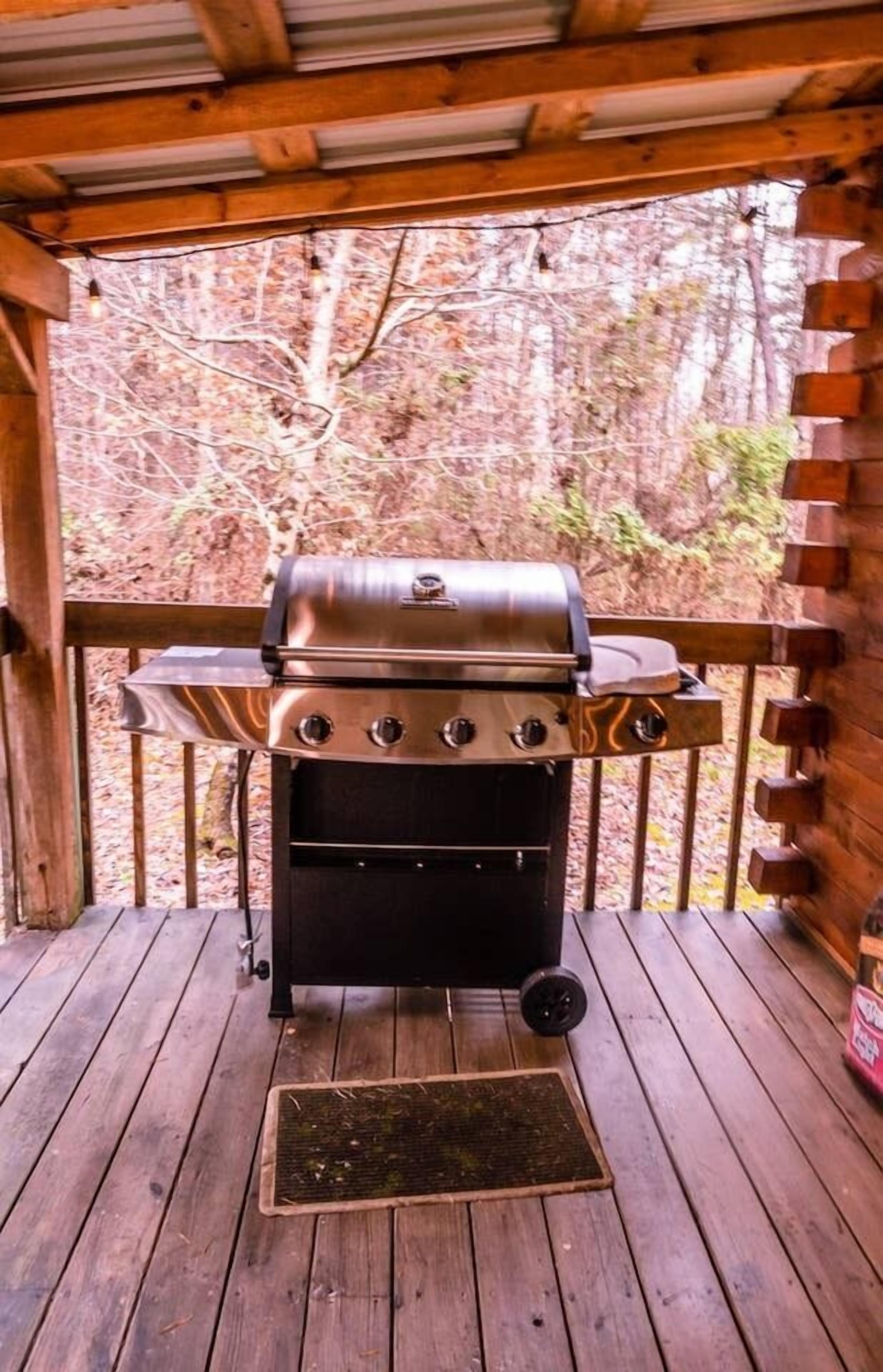 A portable grill on a wooden deck with a view of a wooded area.